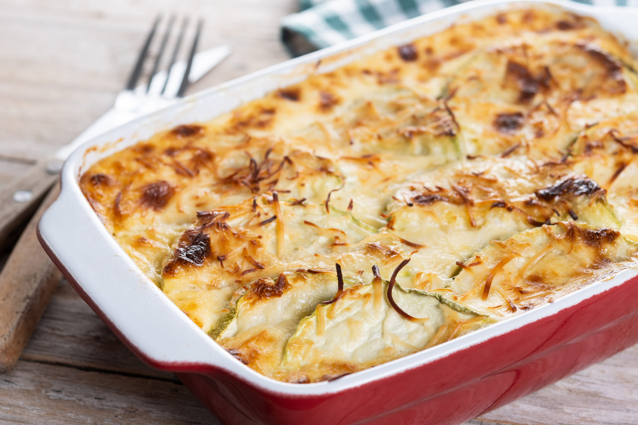 Casserole with cheese and gratin zucchini on wooden table