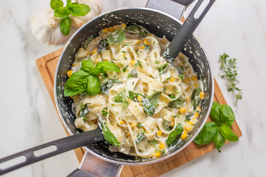 Top view of creamy tagliatelle pasta with herbs and corn in a pot on the table