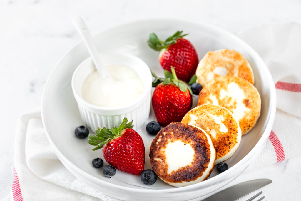 Cottage cheese pancakes, cheesecakes, ricotta fritters with fresh strawberries and blueberries from a white ceramic plate. Healthy and delicious breakfast for the holiday. White background