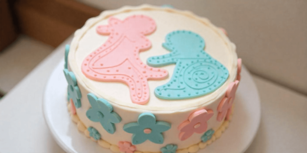 Playful gender reveal cake with baby silhouettes and floral patterns in pink and blue.