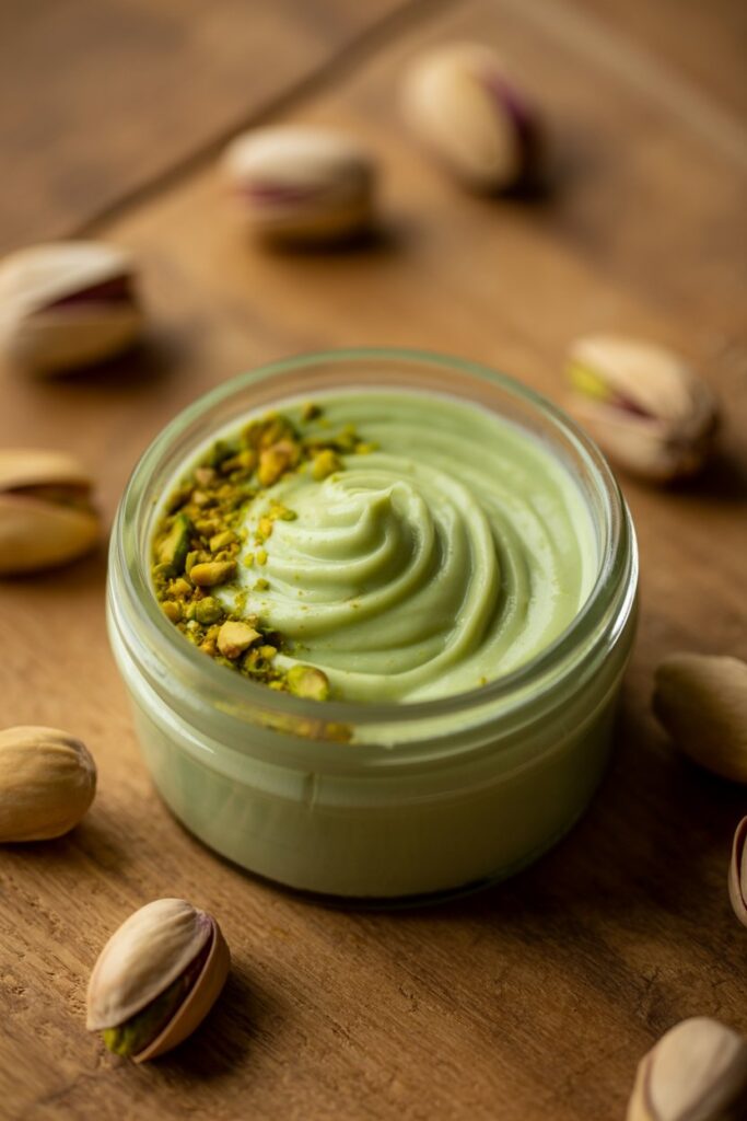 Jar of smooth homemade pistachio cream with fresh pistachios on the side.